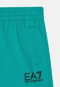 Turkoise joggingbroek met een elastische tailleband, zijzak en zwart EA7-logo. Gemaakt van een zachte, ademende stof met een gladde textuur.