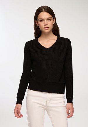 Maglione nero lavorato a maglia con scollatura a V, maniche lunghe e polsini a coste. Il design presenta un tessuto texturizzato e un orlo corto.