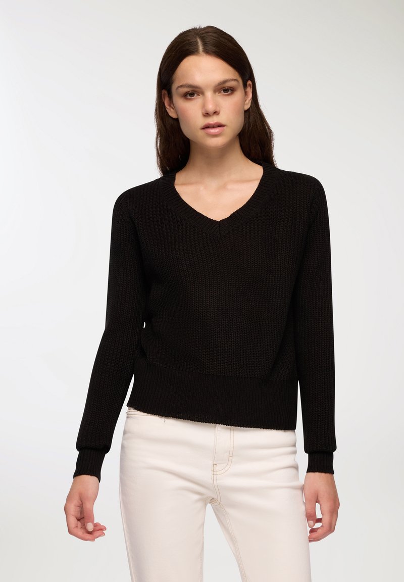 Czarny sweter dziergany z dekoltem w serek, z długimi rękawami i ściągaczami. Projekt cechuje się strukturalnym materiałem i krótkim krojem.
