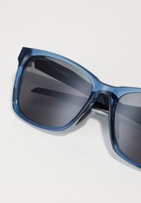 Ochelari de soare din plastic albastru, cu lentile întunecate. Formă pătrată, textură netedă, cu marcajul "PRIZM" pe partea interioară a ramei.