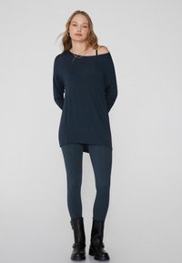 Dunkelblaues Langarmoberteil mit einem schulterfreien Design, kombiniert mit passenden Leggings und schwarzen Knöchelstiefeln. Glatte Textur, lässiger Stil.