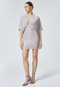 Robe mini brillante de couleur rose avec un décolleté en V profond, des manches chauve-souris et une taille froncée. Présente des pois métalliques et une texture lisse.