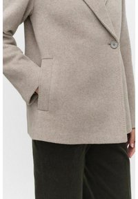 Beige wool-blend jacket with a notch lapel, single button closure, and side pocket. Textured finish, paired with dark green corduroy pants.