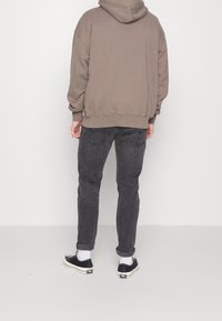 Felpa con cappuccio color taupe, vestibilità comoda; abbinata a jeans grigi slim. Sneakers nere con suole bianche e caviglie risvoltate.