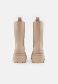 Beige Wildleder-Stiefeletten mit einer strukturierten Oberfläche, dicke Sohlen und einer Schlaufe an der Rückseite; mit vertikalen Nähten für zusätzliche Details.