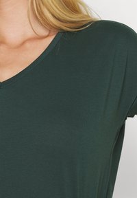 Tmavě zelený top s výstřihem do V vyrobený z měkké, lehké tkaniny s volným střihem, s krátkými rukávy a hladkými, čistými liniemi.