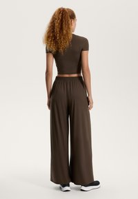 Top scurt maro cu maneci scurte, asociat cu pantaloni larga cu talie elastică în aceeași culoare. Modelul poartă pantofi sport negri.