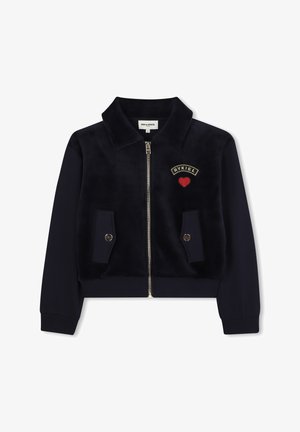 Marineblauwe ritjass met zachte fluwelen stof en twee voorzakken, met een geborduurd "RYKIEL" logo en een rood hartje. Accenten van gouden hardware.