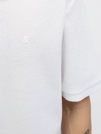 Witte gestructureerde polo met korte mouwen en een klein reliëflogo op de borst. De stof heeft een wafelbreipatroon.