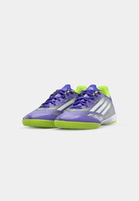 Scarpe sportive viola con accenti verdi, dotate di una tomaia texturizzata, tre strisce bianche e un design leggero per agilità e supporto.