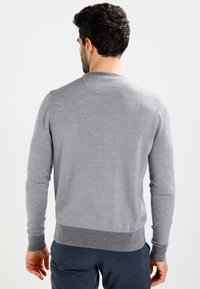 Maglione grigio con collo rotondo e polsini e fondo a costine. Realizzato in un morbido materiale lavorato a maglia, presenta una superficie liscia e un design aderente.