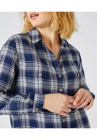Camicia a scacchi navy con bottoni, a strisce bianche e grigie, con due tasche sul petto e bottoni dorati. Tessuto morbido e maniche lunghe.