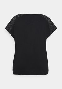 Camiseta negra de corte holgado, con acentos de malla negra texturizada en el hombro, escote redondeado y mangas cortas y anchas.