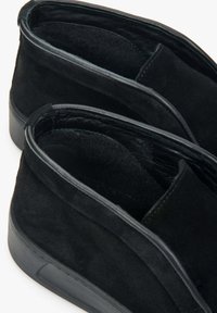 Czarne zamszowe buty wsuwane z niską gumową podeszwą, z miękkim wyściółką, okrągłym noskiem i minimalistycznymi detalami szycia.