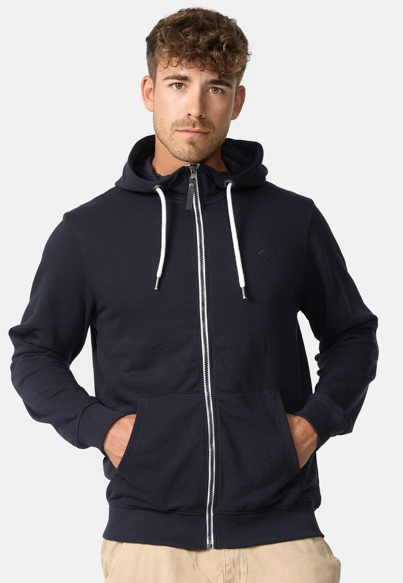 Navy plavi zip-up dukserica od mekanog materijala, s prednjim džepon, bijelim vezicama i malim logotipom na prsima.