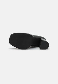 Black high-heeled shoe with a smooth leather upper, square toe, and a textured rubber sole. Heel features a chunky design for stability.
