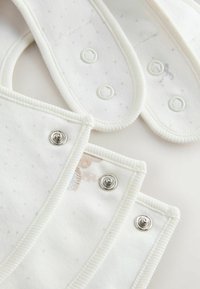 Bomullshaklappar i vitt med silverfärgade tryckknappar. Texturerad tygt med små prickiga mönster och subtila grafiska inslag.