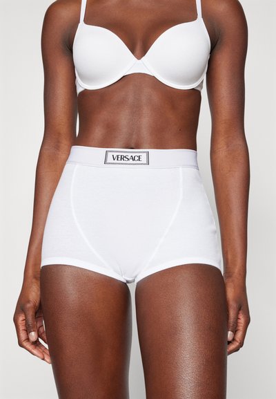 Bragas blancas de talle alto hechas de una tela suave con un acabado liso. Presentan un logo negro de Versace en la cinturilla y costuras limpias.