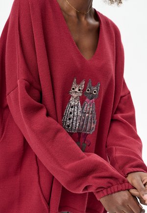 Czerwony sweter dziany o luźnym kroju, z haftowanym motywem dwóch kotów w wzorzystych sukienkach. Dekolt w serek i elastyczne mankiety.