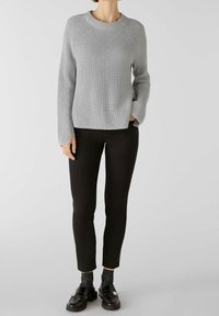 Suéter de canalé gris claro con cuello redondo y mangas largas, combinado con pantalones negros ajustados y mocasines negros con detalle de hardware.