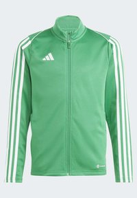Giacca verde con zip realizzata in tessuto liscio, con accenti bianchi a tre strisce sulle maniche e un colletto alto. Logo Adidas sul petto.