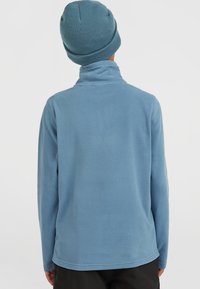 Lyseblå fleecepullover med høj krave og lange ærmer, der har en glat tekstur og en tætsiddende silhuet. Sammen med en matchende hue.