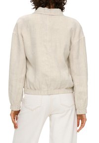 Light beige linen jacket with a collared neck, elasticized waistband, and slightly oversized fit. Features dropped shoulders and cuffed sleeves.