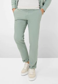 Helle grüne Hose aus glattem Stoff mit schmaler Passform, vorderen Taschen und aufgeschlagenen Säumen, getragen mit beigen Sneakers.