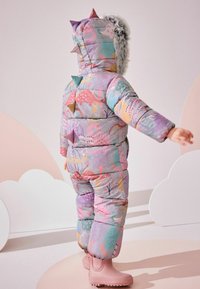 Gepolsterter Schneanzug in Multicolor mit Tier- und Blumenmustern. Verfügt über eine mit Fleece gefütterte Kapuze und bunte Stacheln auf dem Rücken. Passt zu rosa Stiefeln.