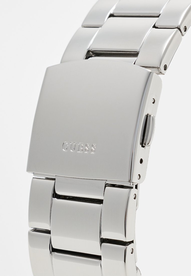 Reloj de acero inoxidable plateado con acabado pulido, caja rectangular, pulsera de eslabones y logo grabado "GUESS" en el cierre.