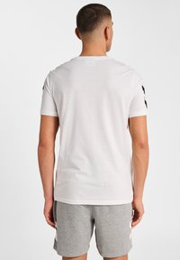 Vit t-shirt med kort ärm och rund halsringning, med svarta detaljer på axlarna. Tillverkad av mjukt material, har den en avslappnad passform.