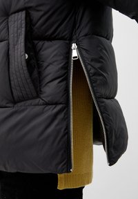 Czarna kurtka puchowa o pikowanej fakturze, z metalowymi suwakami w kolorze srebrnym oraz kontrastową, oliwkową podszewką z dzianiny.