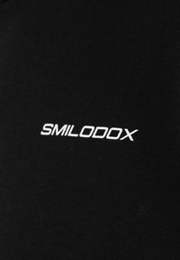 Logo blanc "SMILODOX" imprimé sur tissu noir.