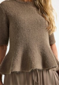 Top peplum in misto lana marrone con maniche corte, finitura testurizzata e scollatura ampia. Indossato sopra una gonna marrone chiaro con cordoncino.