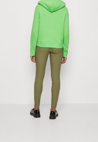 Sudadera verde con un bolsillo canguro en la parte frontal, combinada con leggings verde oliva. Unos zapatos de plataforma negros completan el conjunto. Tejido suave y elástico.