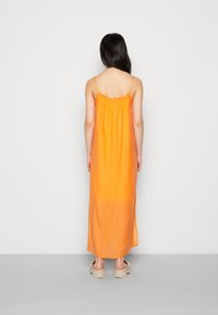 Vestido maxi laranja com alças finas e decote franzido. Feito de um tecido leve, apresentando um corte solto e aberturas laterais. Usado com calçado bege.