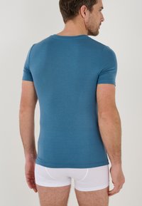 T-shirt aderente a maniche corte in un misto cotone blu, con scollatura rotonda e texture liscia, indossato con slip bianchi.