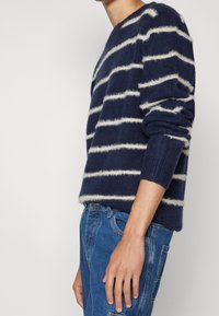 Marinblårandig tröja i mjukt, fluffigt material; har vita horisontella ränder, rund halsringning och ribbade ärmslut; bärs med blå jeans.