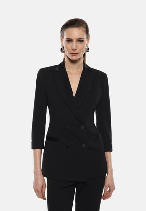 Blazer nero doppiopetto con lapel affilati, maniche a tre quarti e tasche frontali; texture liscia con un sottile lucido.