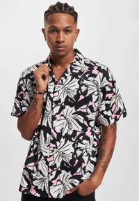 Camisa de manga corta con un patrón floral en negro, rosa y blanco, con diseño de cuello y botones de madera, confeccionada en una tela ligera.