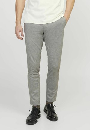 Pantaloni grigi scampanati con un tessuto testurizzato, caratterizzati da un motivo sottile. Abbinati a scarpe eleganti nere e a una maglietta di colore chiaro.