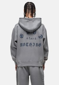 Felpa con cappuccio grigia con testo blu "GOD for NOTHING" sul retro. Vestibilità casual con polsini e orlo a coste. Realizzata in tessuto morbido.