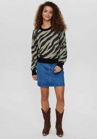 Črno in kremno zebra-motivirano pulover z rebrastimi manšetami in robom, v kombinaciji z modrim denim krilom in rjavimi kavbojkami.