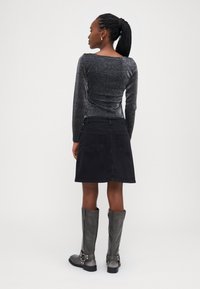 Svart denimskjørt med baklommer, kombinert med en gl shiny, mørkegrå langermet topp. Grå knelange støvler med spenneakcenter.