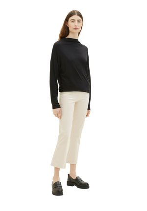 Zwarte lange mouw top met een hoge hals, gecombineerd met crèmekleurige flared broek. De schoenen zijn zwarte leren instappers met dikke zolen.