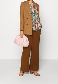 Blazer marrone doppiopetto sopra una blusa floreale rosa, abbinato a pantaloni larghi marroni, sandali beige e una borsa a tracolla rosa chiaro.