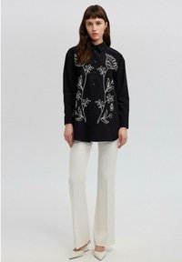 Black button-up shirt with white floral embroidery. Paired with white flared pants and light-colored pointed-toe shoes. Simple design, tailored fit.