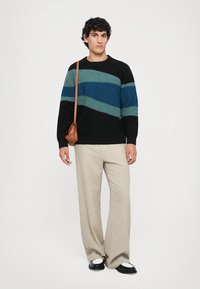 Pulover tricotat cu dungi negre și teal, cu textură ribbed, asortat cu pantaloni pliați bej și pantofi negri, complementat de o geantă maro tip crossbody.