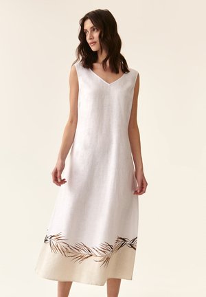 Weißes Leinenkleid mit V-Ausschnitt und ärmellosem Design. Mit braunem, gesticktem Blattmuster nahe dem Saum. Ausgestellte A-Linien Silhouette.