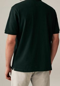 Ciemnozielona koszulka polo z krótkim rękawem, wykonana z bawełny, z klasycznym kołnierzykiem, prostym dołem i bocznymi rozporkami dla swobody ruchów.